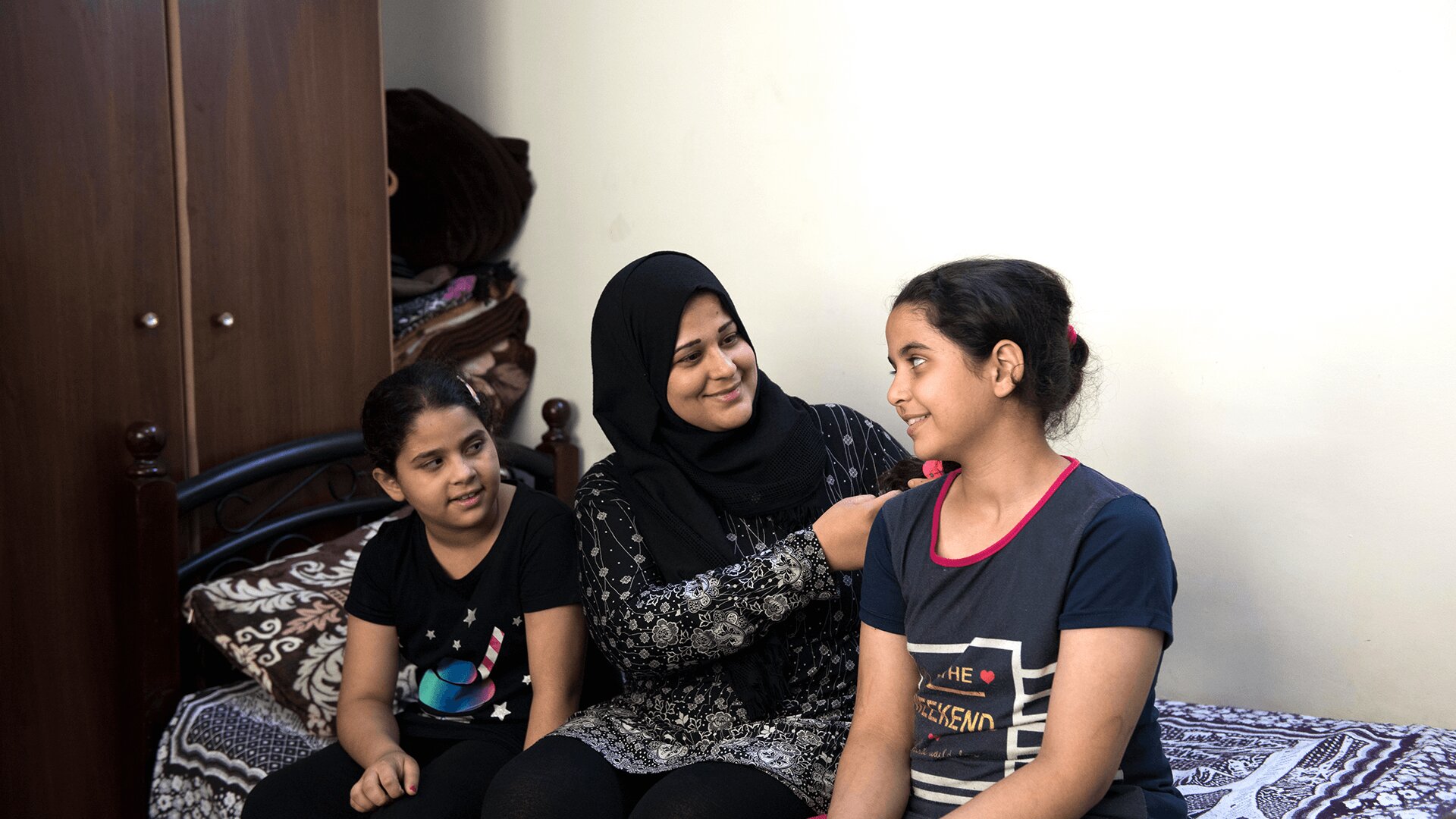 Hanaa and her two daughters sit on a bed 