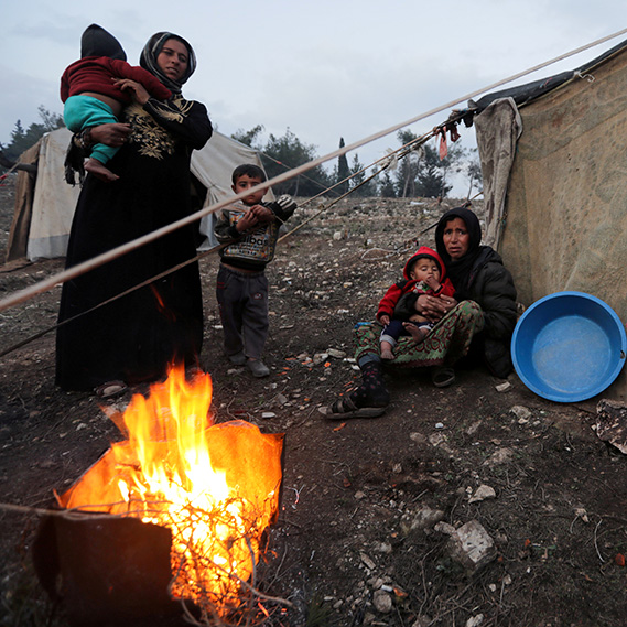 A Syrian woman and her children gather around a fire after fleeing southern Idlib