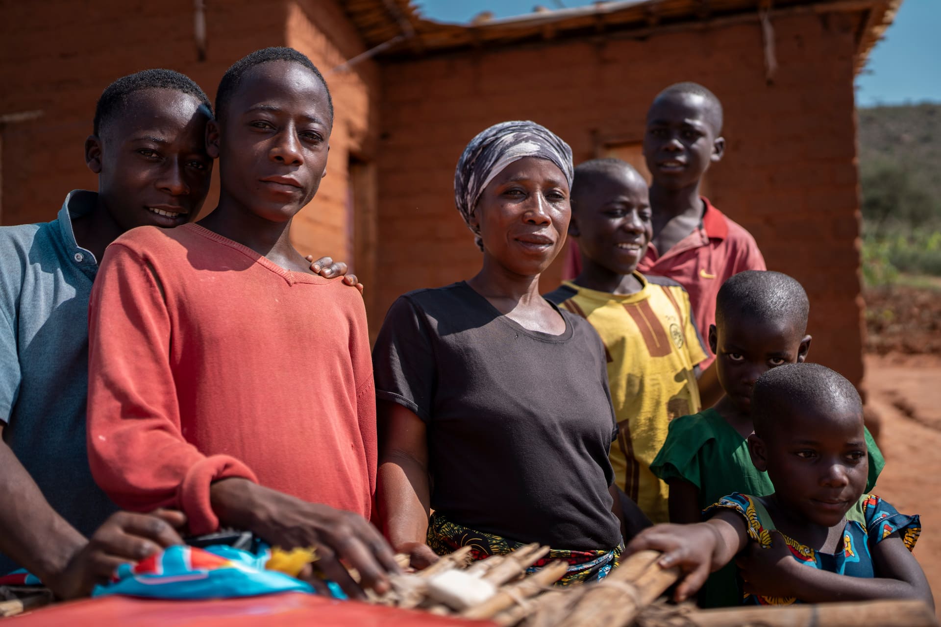 Obed*, 17 (wearing a red jumper), stands in a group photo with his mother, Bercia*, and his siblings outside their shelter in Nakivale