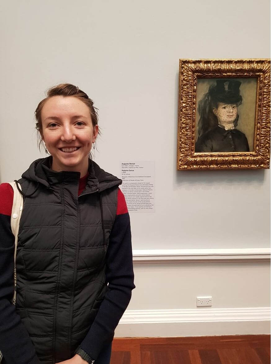 Sophie Forest stands in front of impressionist artwork 