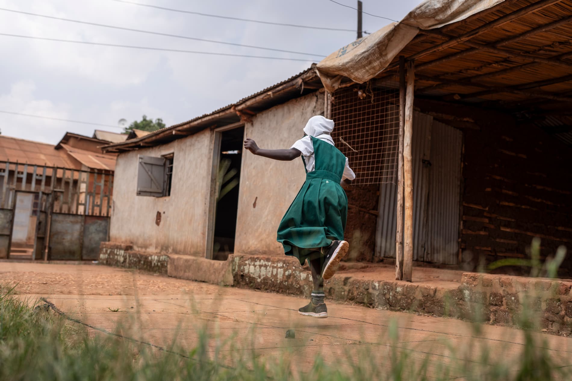 A refugee girl in a green school uniform plays a game in the yard of her home in Kampala, Uganda