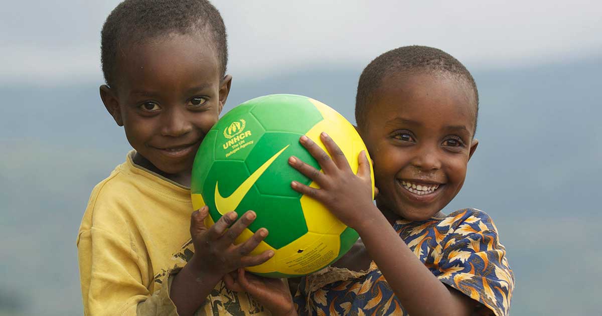 Two young children hug a soccer ball, smiling. 