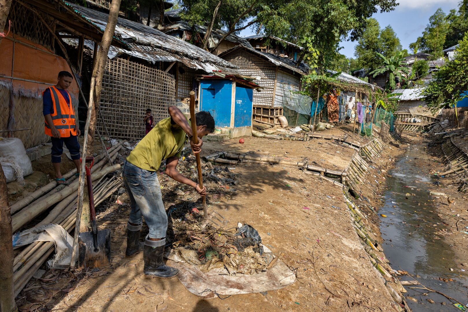 A young man uses a rake to gather rubbish from a dirty stream in Cox's bazar, Bangladesh